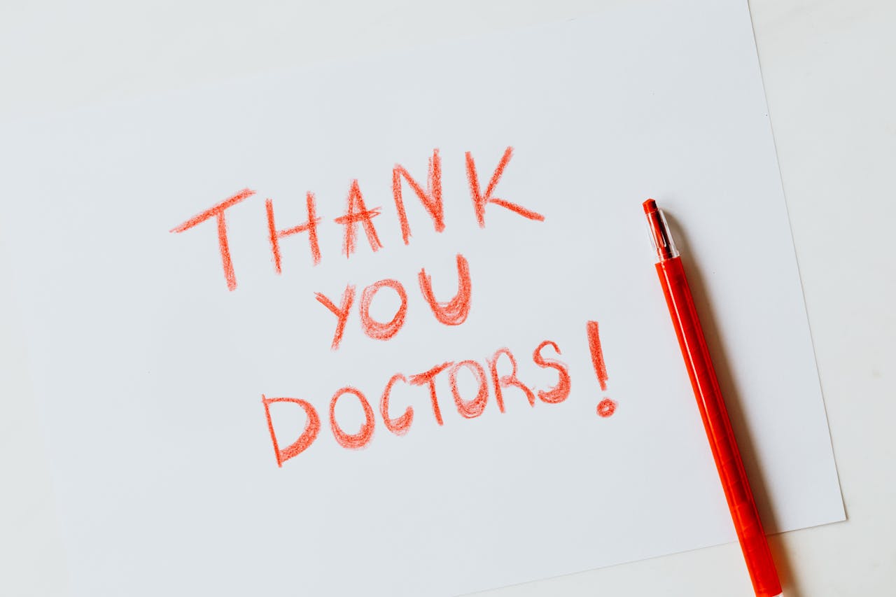 A heartfelt handwritten 'Thank You Doctors' note in red on white paper with a matching red pencil.