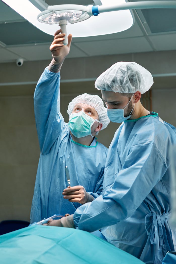 Two surgeons in an operating room adjusting lights and preparing for surgery in sterile attire.